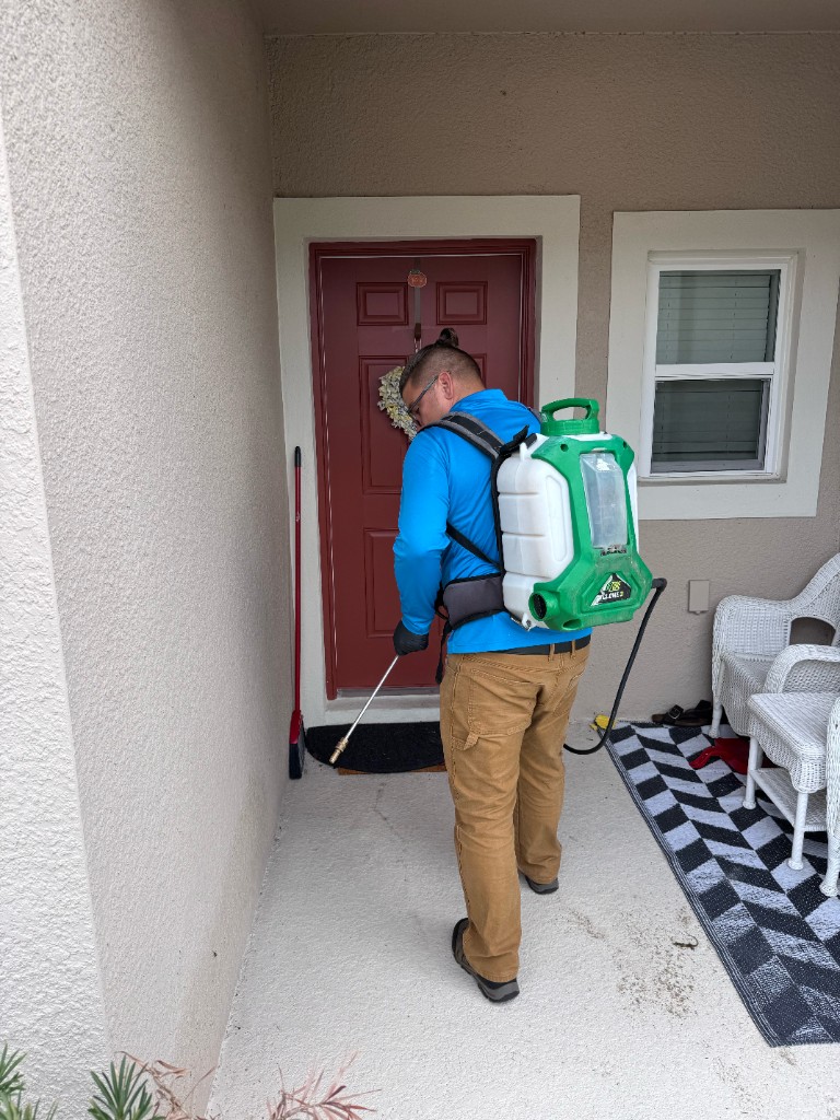 Technician performing perimeter pest treatment at a residential entry